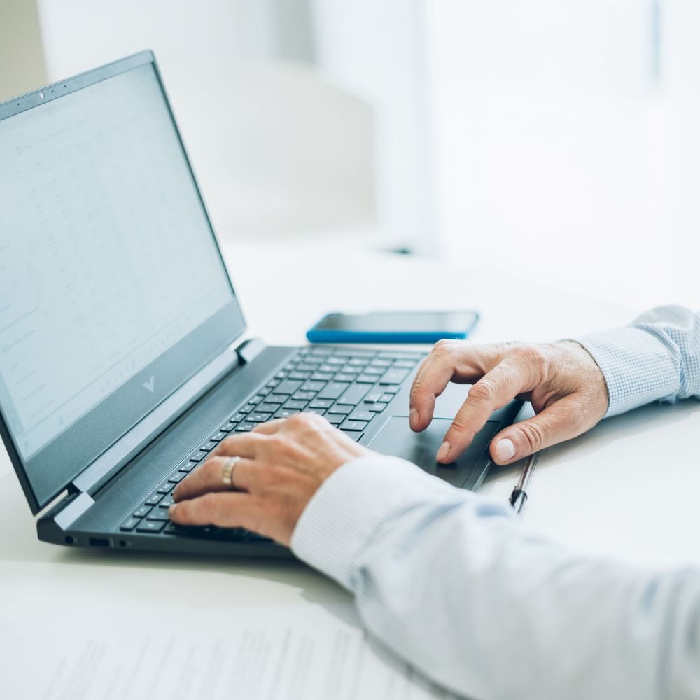Close-up of hands typing on laptop keyboard on white desk surface.