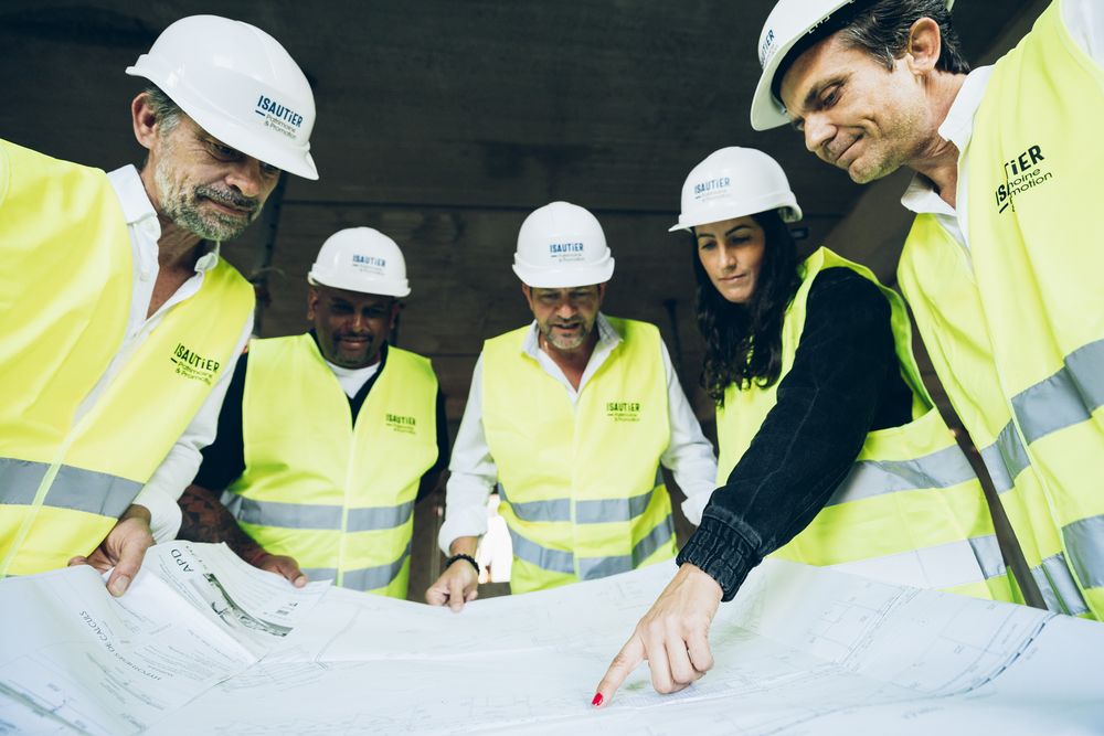 Construction team in hard hats and high-visibility vests reviews blueprints on a table during project planning meeting.