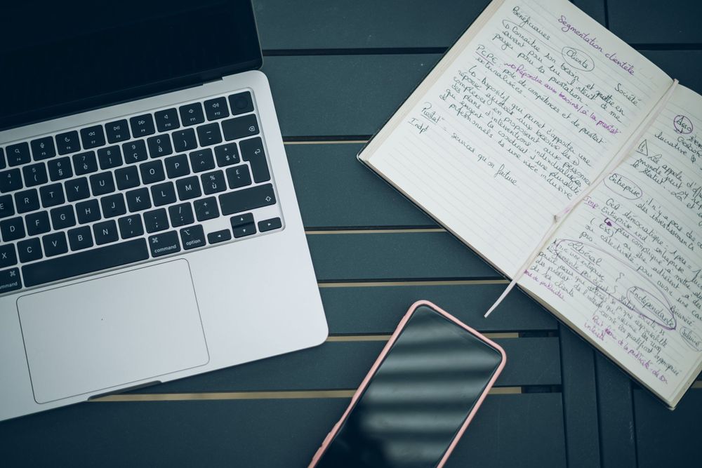 Laptop computer, smartphone and handwritten notes on a dark wooden surface.