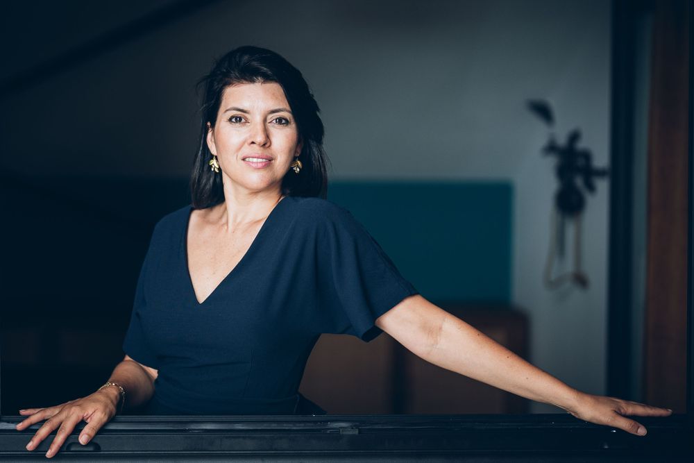Portrait in professional formal setting with navy blue v-neck dress against dark moody background.
