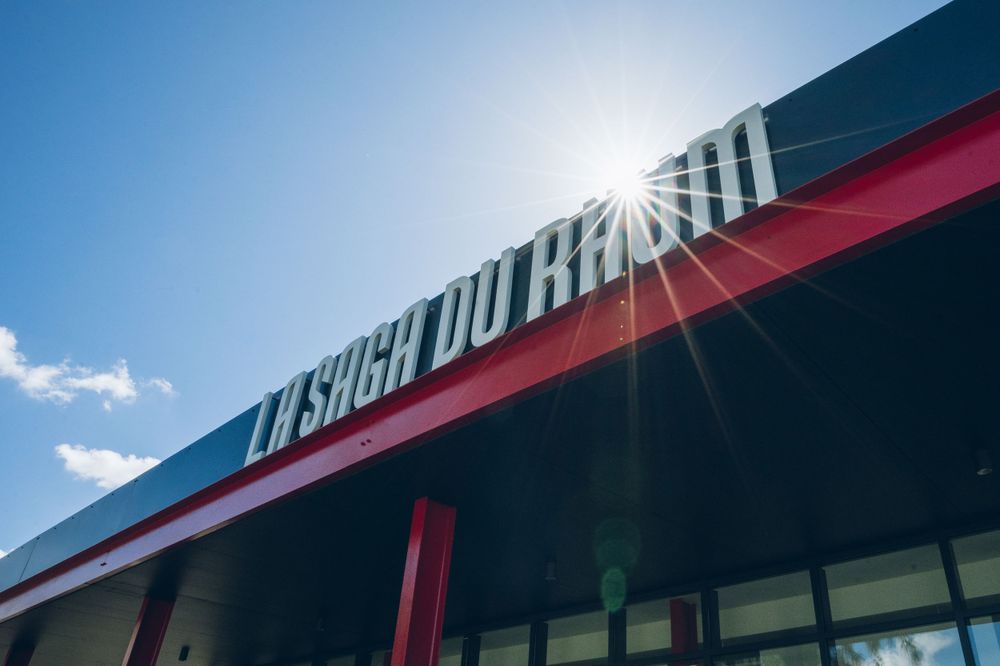 Sunlit storefront sign reading 'La Salle Du Hibou' against a blue sky with sun flare.