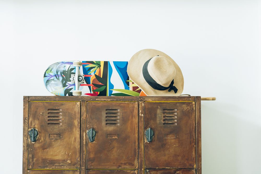 A vintage industrial rusty metal locker with storage items and a straw hat on top against a white wall.