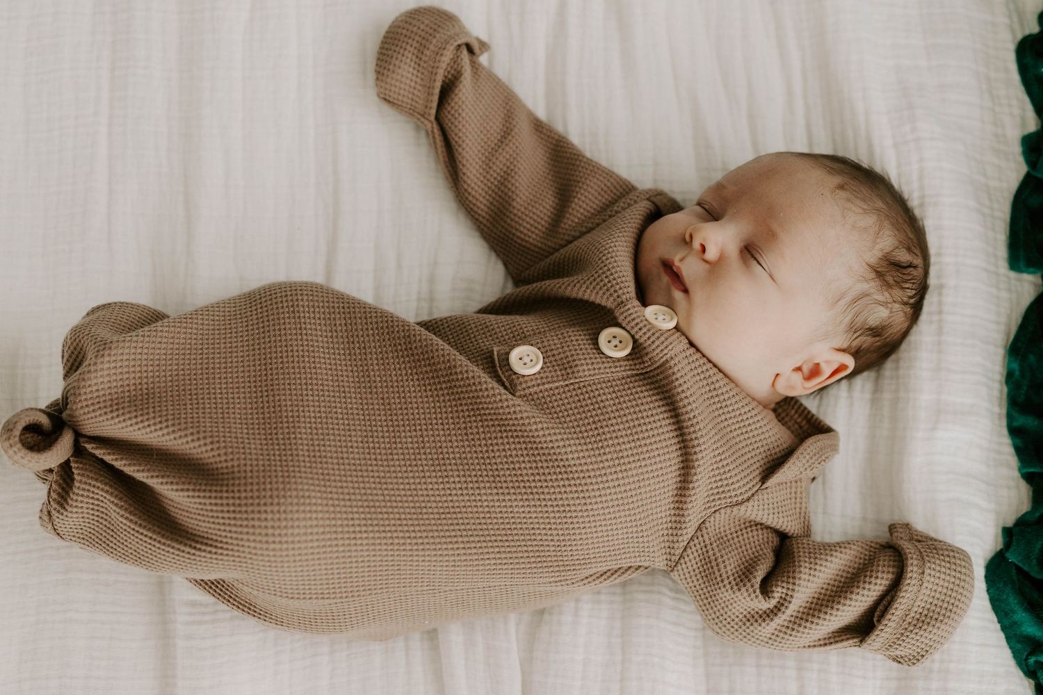Baby sleeping peacefully in brown knit romper on white bedding.
