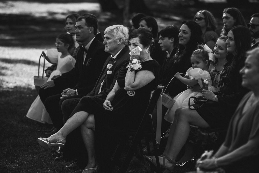 Wedding guests seated outdoors watching ceremony with joyful expressions.