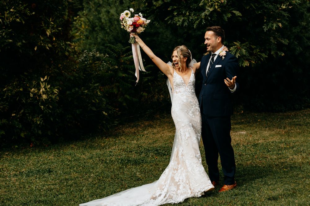 Wedding couple dances joyfully on grassy outdoor venue.