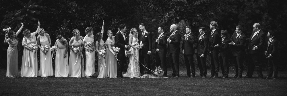 Wedding party lined up in formal attire against dark outdoor background.