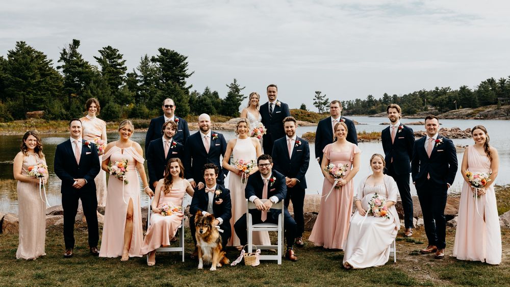 Wedding party relaxes on waterfront with bridesmaids in blush pink dresses.