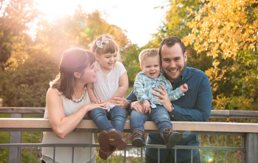 Family sitting together on railing during golden hour with autumn trees in background.