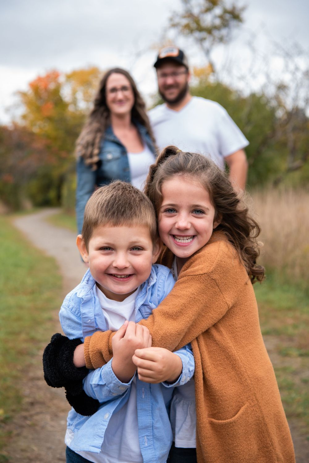 A happy family shares laughter together on an autumn path surrounded by fall foliage and natural scenery.