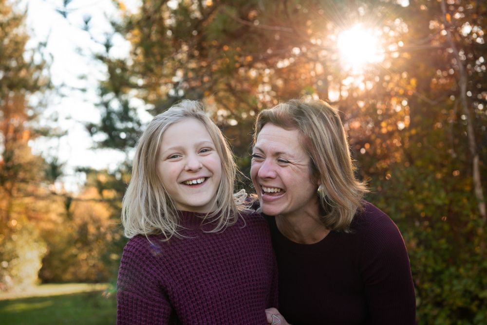 Two people share genuine laughter during golden hour in an autumn outdoor setting with sunlit trees in background.