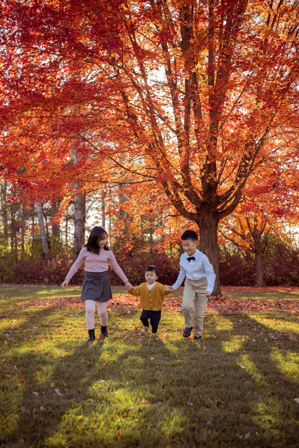A group holds hands while walking under vibrant red autumn foliage.