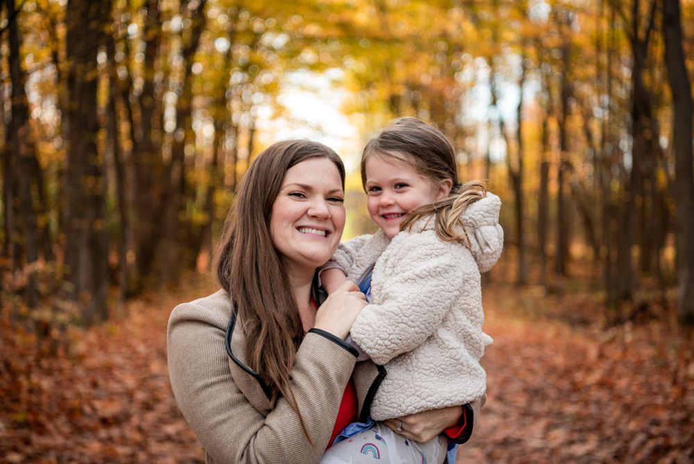 Two people share a loving embrace while surrounded by golden autumn foliage in a forest setting.