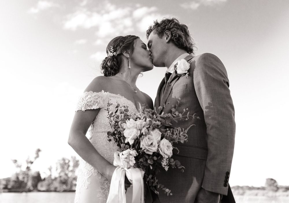 Romantic black and white wedding portrait of a couple kissing while holding a bouquet of flowers.