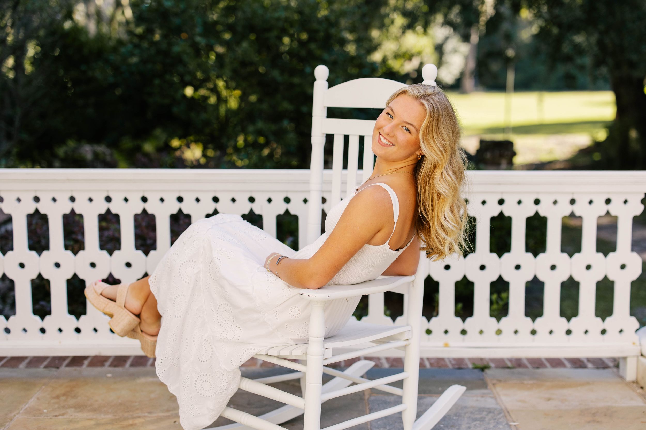 A woman in athletic wear performs stretching exercises on a white porch with a picket fence in the background.