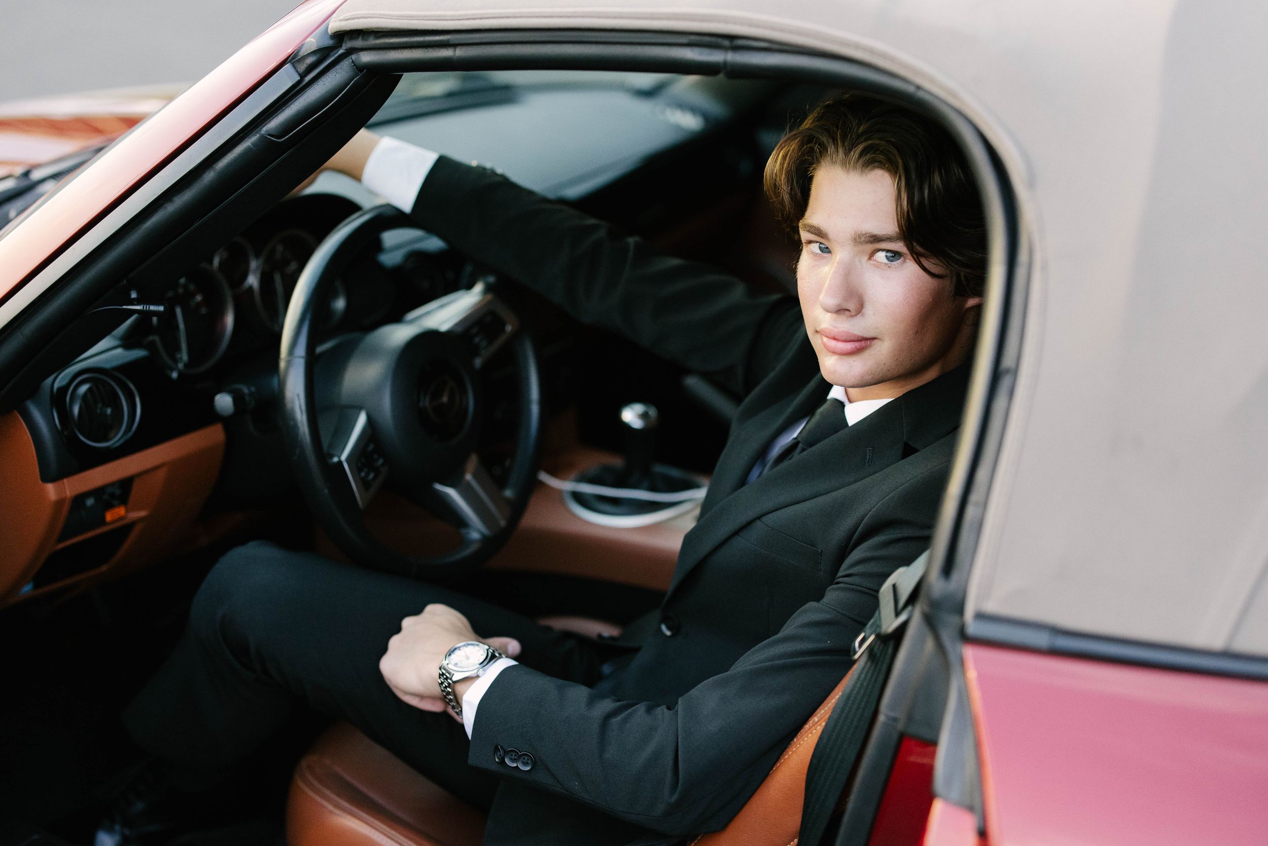 Person sitting in driver's seat of car wearing black coat while looking ahead through windshield.