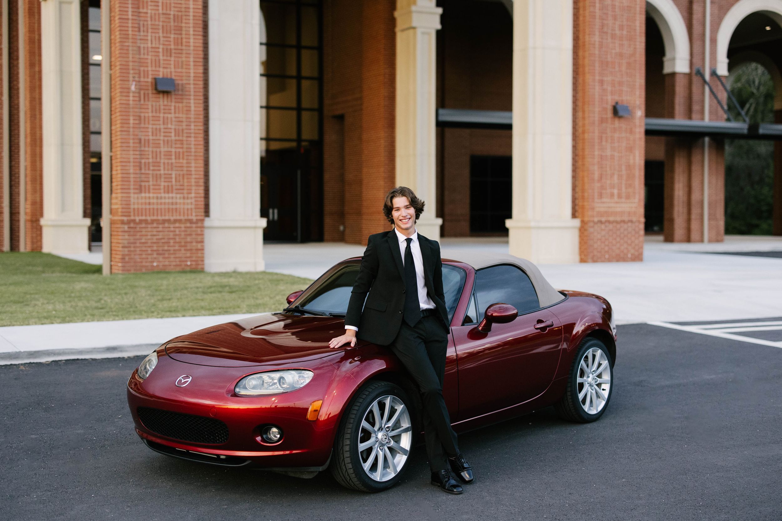 A burgundy Chevrolet Corvette C6 sports car parked in front of a brick building.