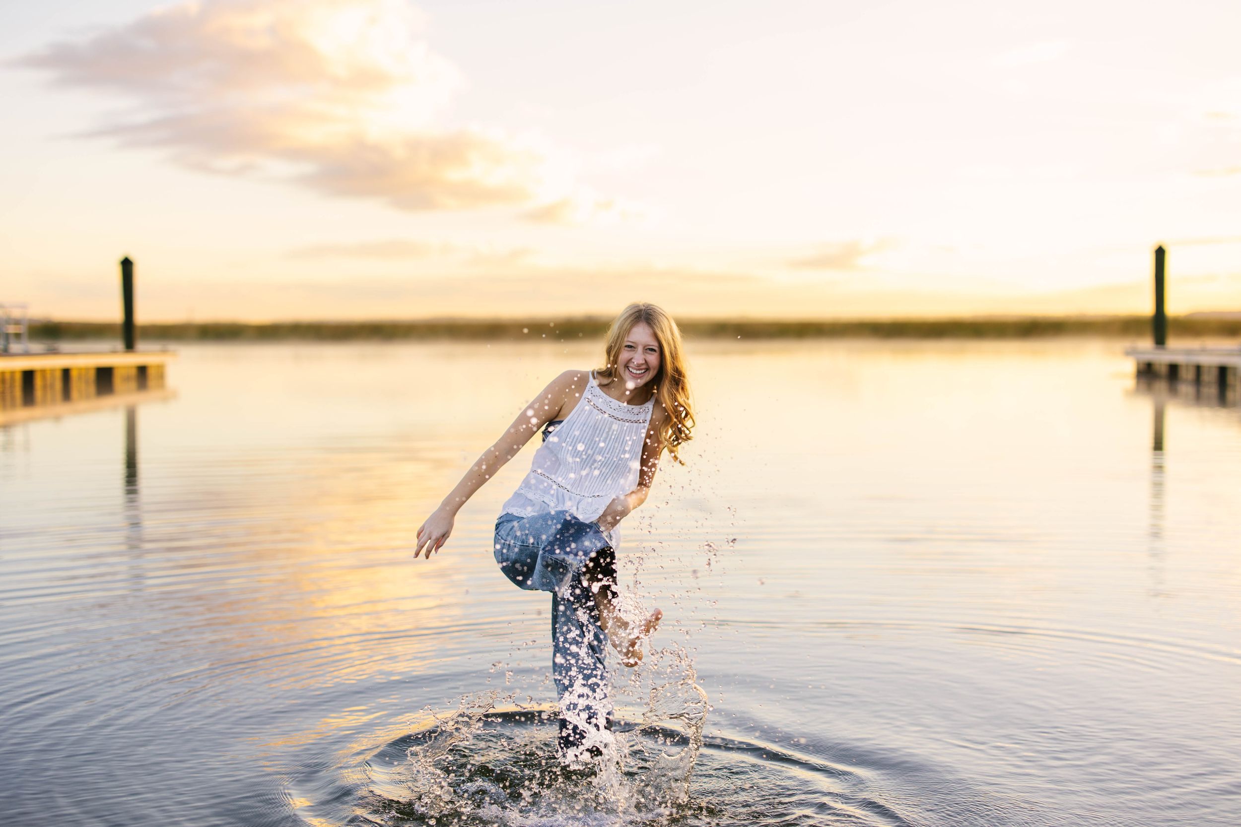 A person splashes through shallow coastal waters during golden hour at sunset.