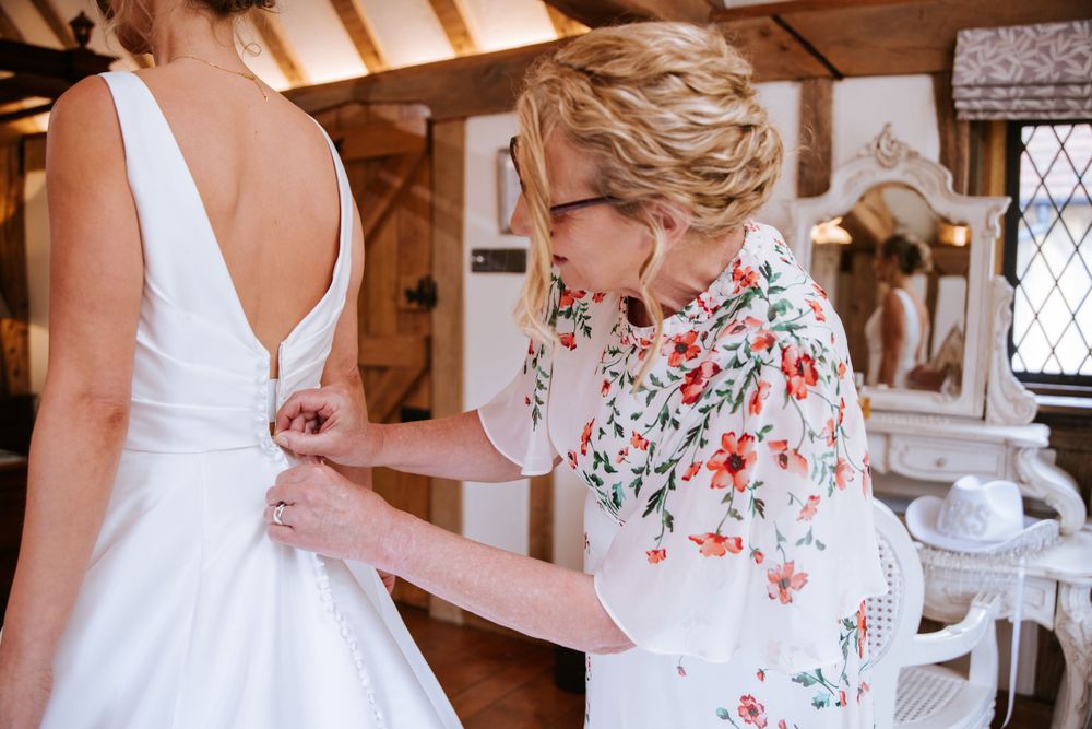 Bride's mother helping with wedding dress buttons during bridal preparations in Cain Manor, Hampshire.