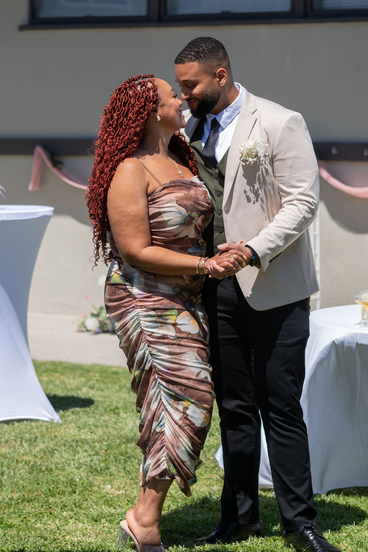 A couple shares a romantic dance outdoors at a wedding reception, man in tan blazer, woman in floral dress.