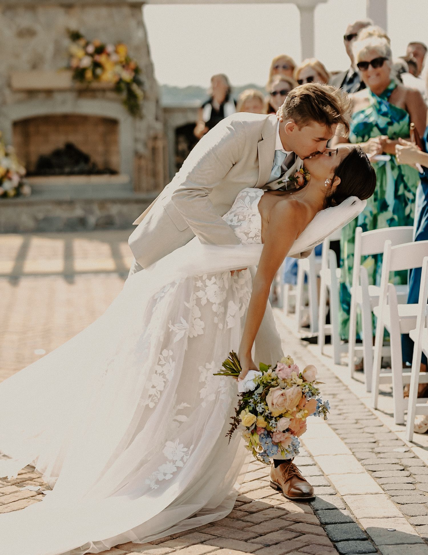 Bride and groom sharing a romantic dip kiss in the aisle at an outdoor wedding ceremony.