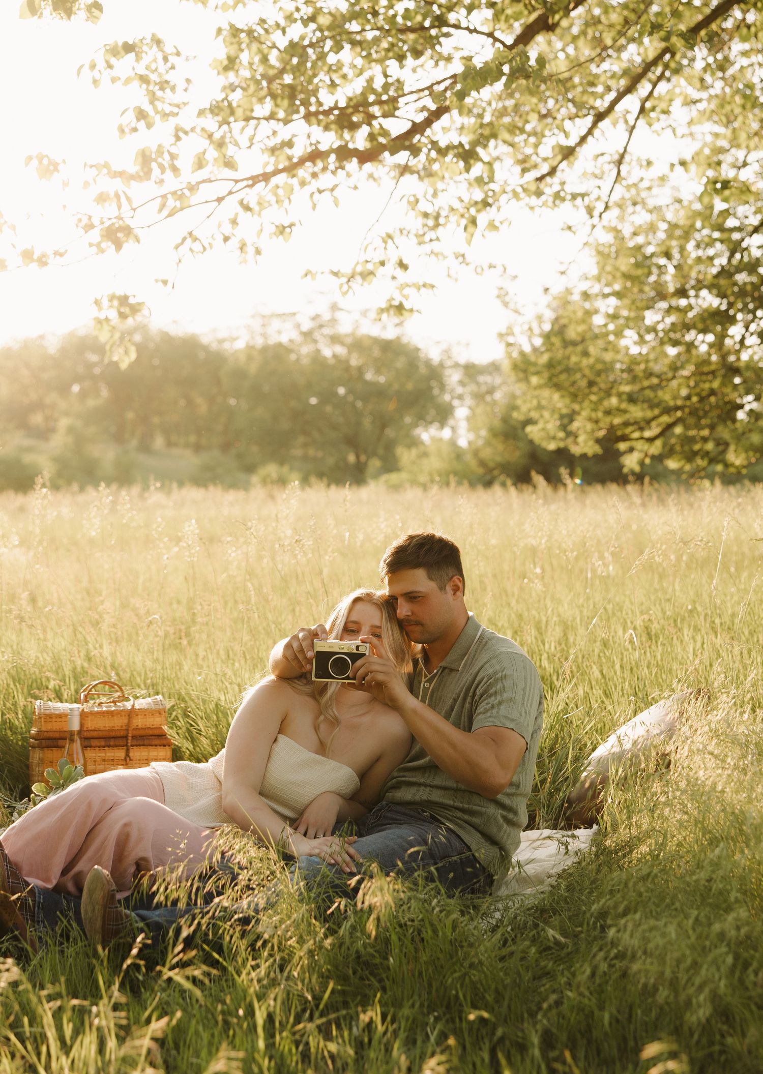 A couple enjoys a romantic picnic in a golden wheat field at sunset with a wicker basket and blanket spread out.