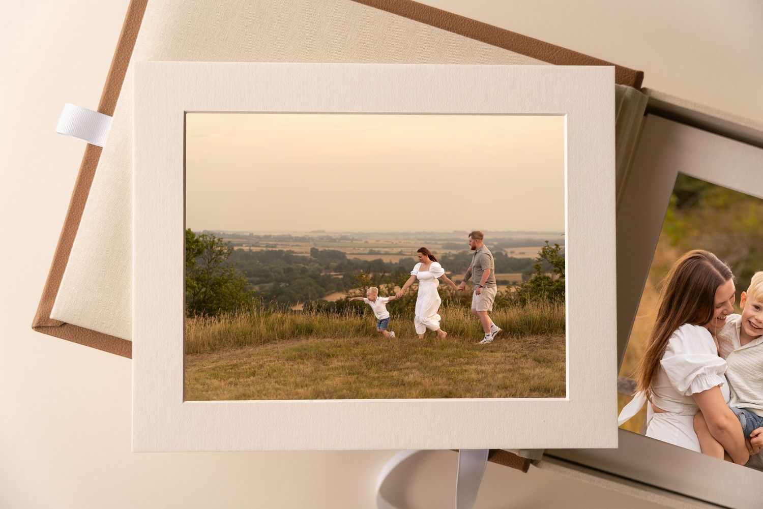 Matted family photo print of parents and a child walking through a grassy field at sunset, displayed in a keepsake photo box.