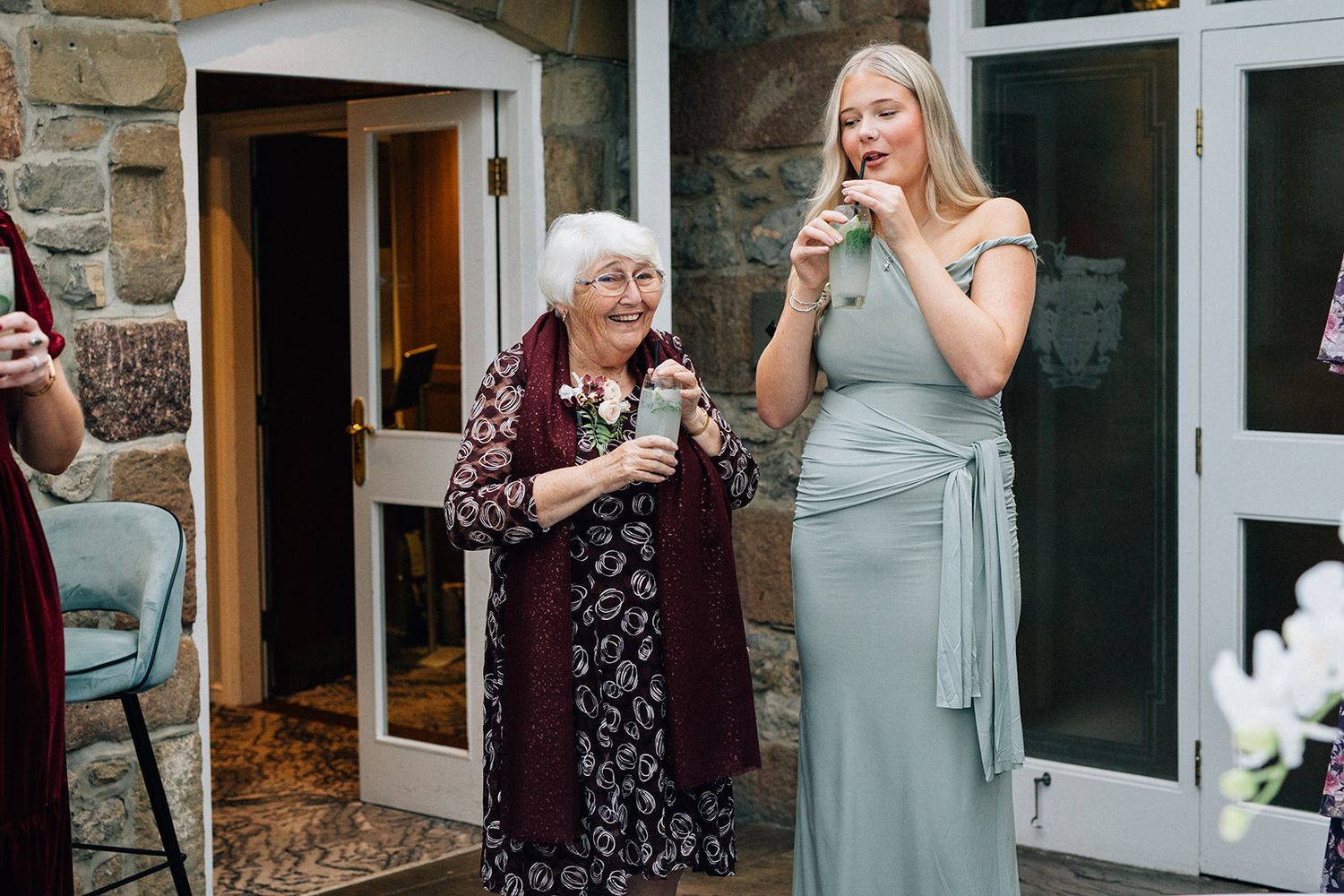 Elderly woman in a floral dress and burgundy cardigan smiles beside a woman at the coniston hotel near Skipton, during a wedding