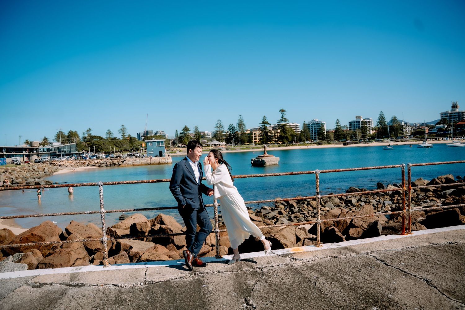 Bride and groom embrace on a seaside promenade by calm blue water - intimate coastal elopement