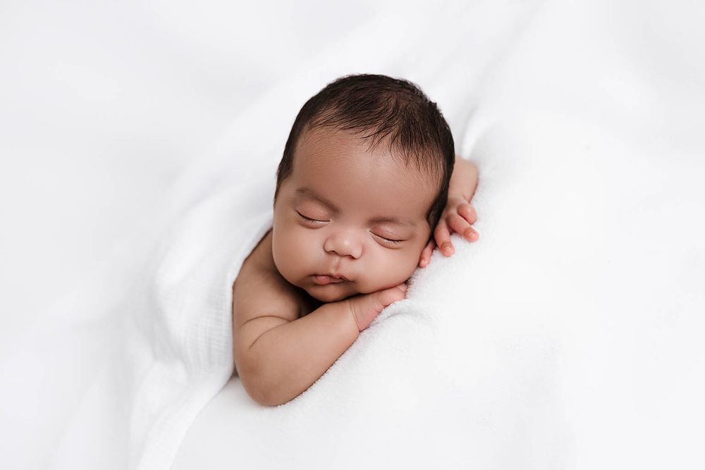 Peaceful newborn baby sleeping wrapped in soft white blanket.