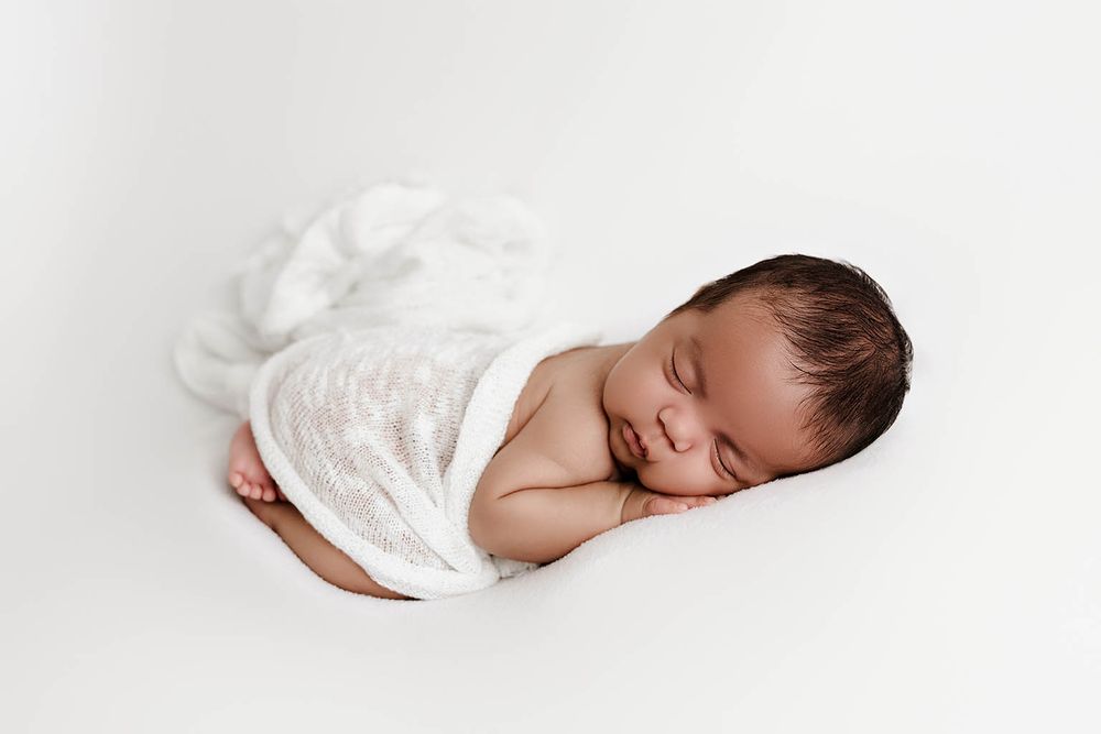 Peaceful newborn baby sleeping wrapped in white lace swaddle on white background.