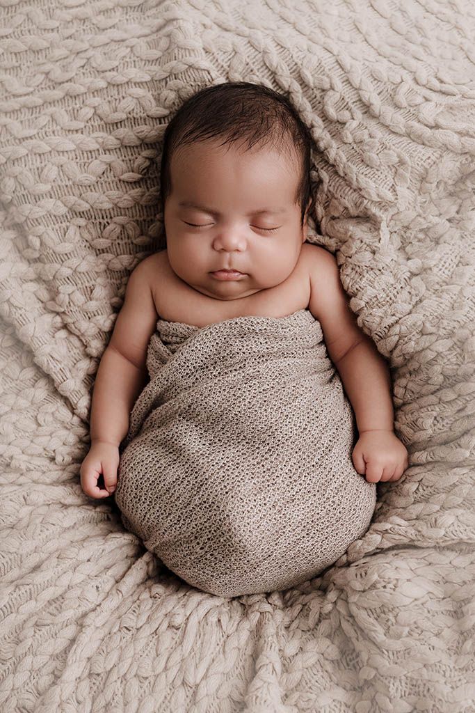 Peaceful newborn baby swaddled in a soft beige knit wrap, sleeping on a cozy textured blanket.