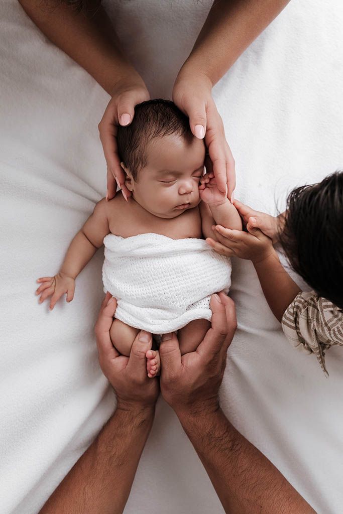 Parents tenderly cradling their sleeping newborn baby wrapped in white on a soft blanket.