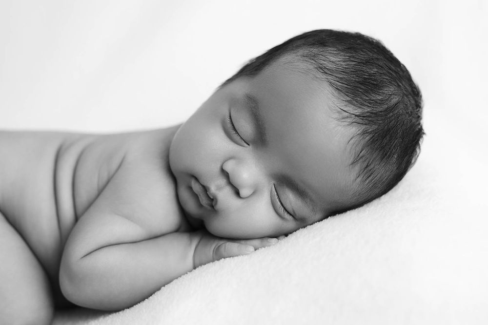 Black and white photo of a peaceful sleeping newborn baby resting on a soft white blanket.