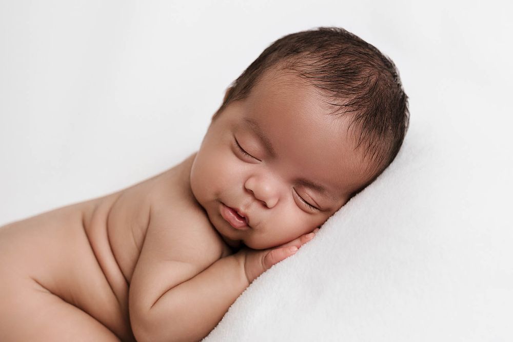 Serene newborn baby sleeping on white blanket with hands under cheek.