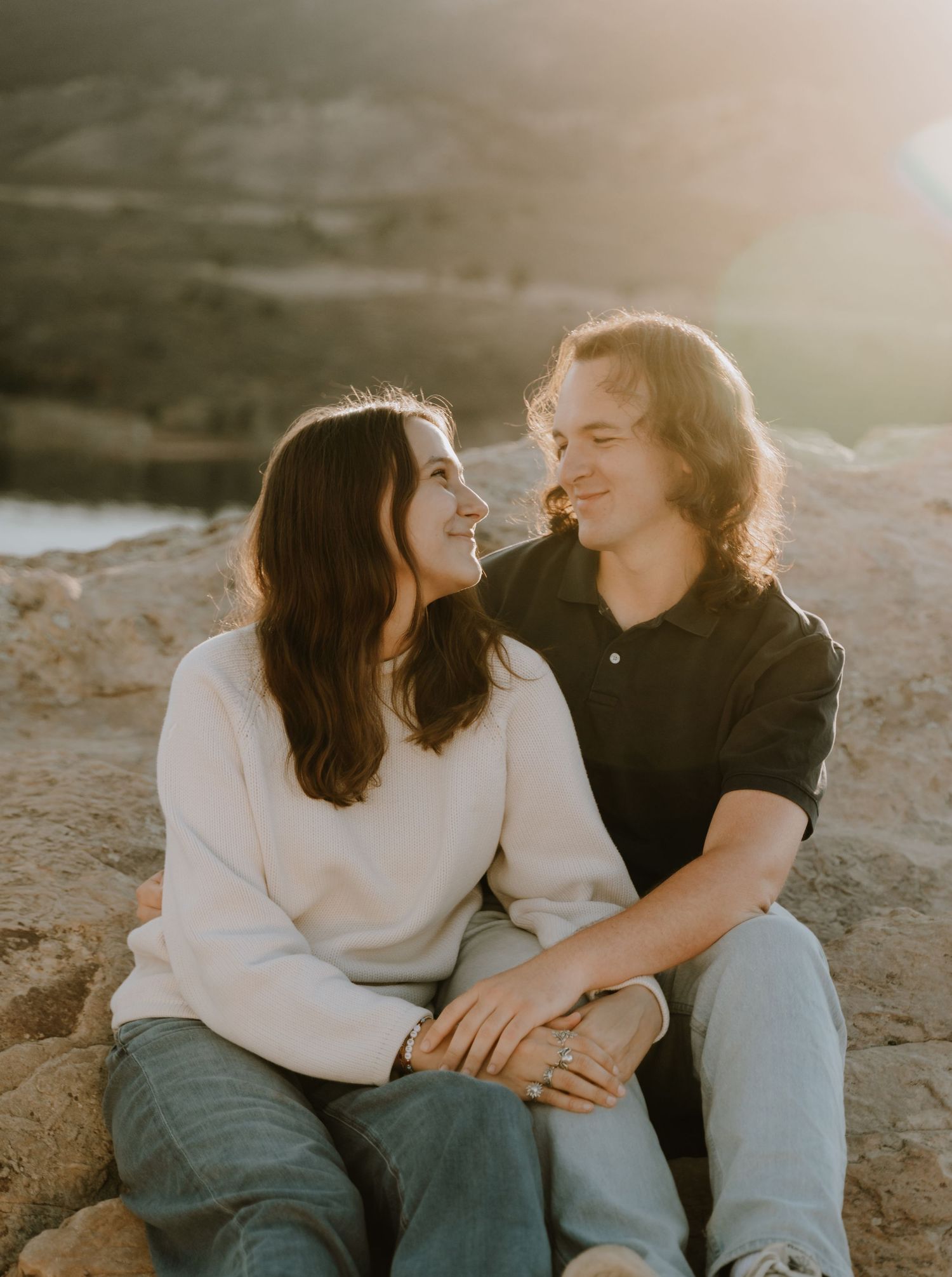 Couple looks at each other with love and sit together on a rock with an artistic sun flare
