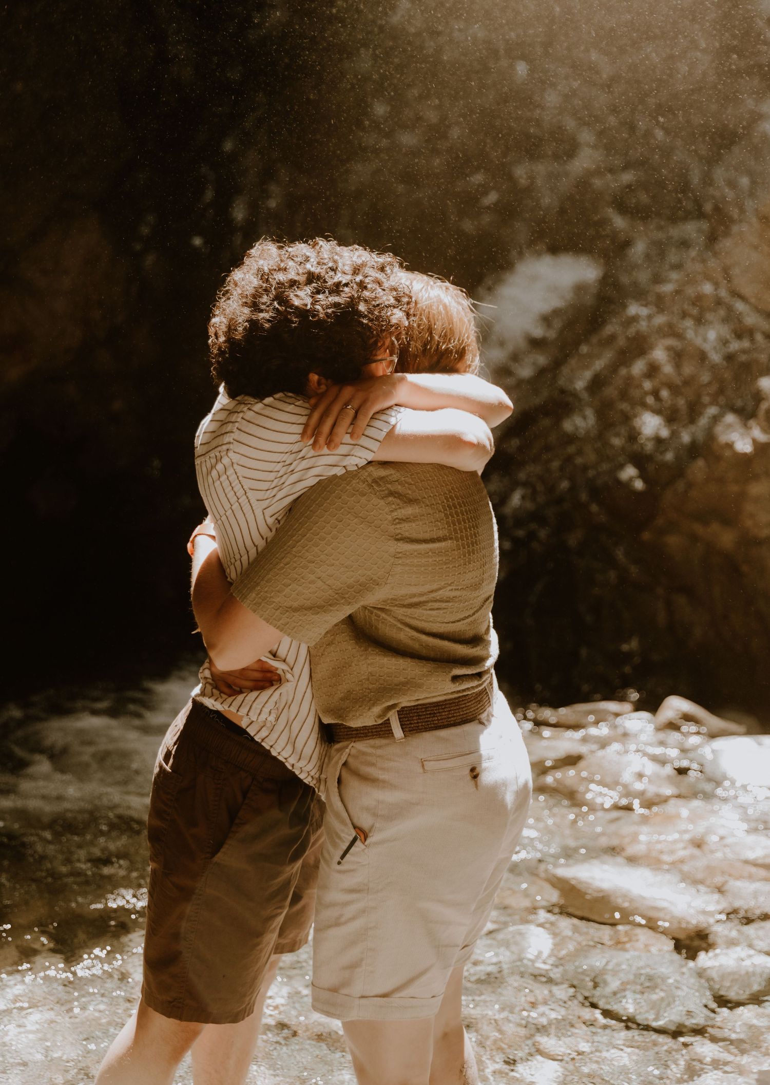 Couple looks at each other with love and sit together on a rock with an artistic sun flare