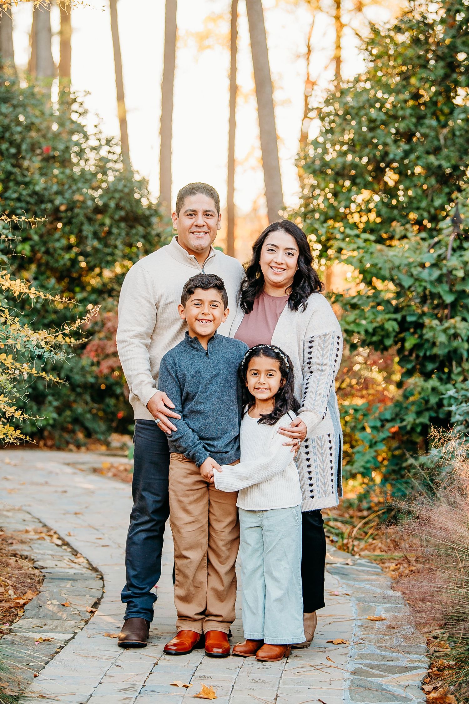 A family of four poses on a garden path surrounded by fall foliage.