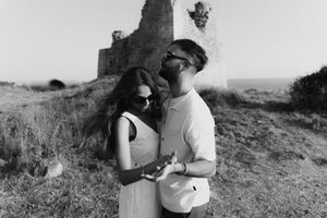 Black and white photo of couple embracing near ancient castle ruins on a sunny day.