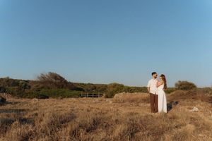 Romantic couple embracing in a golden dry meadow under a clear blue sky in a serene outdoor setting.