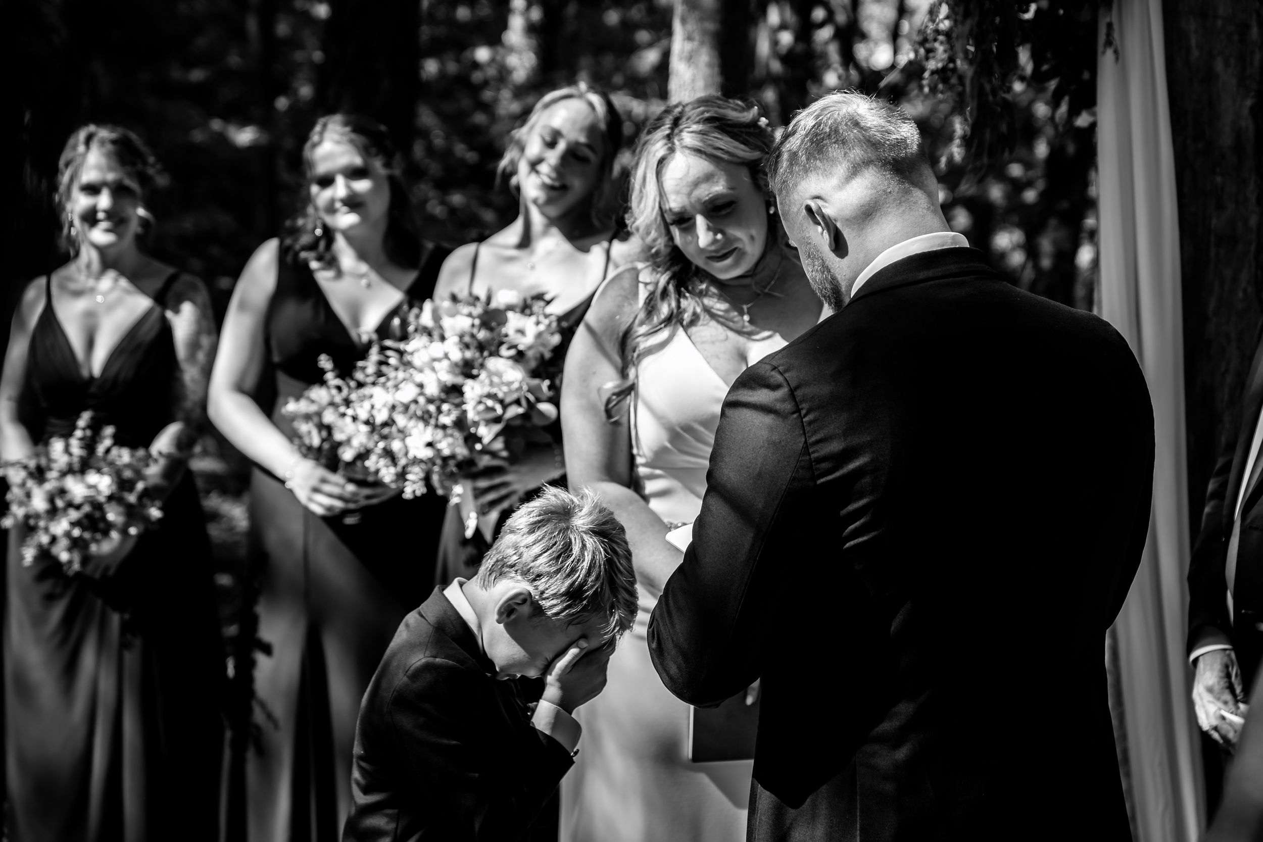 Emotional black and white photo of bride receiving ring from groom at outdoor wedding ceremony with bridesmaids.