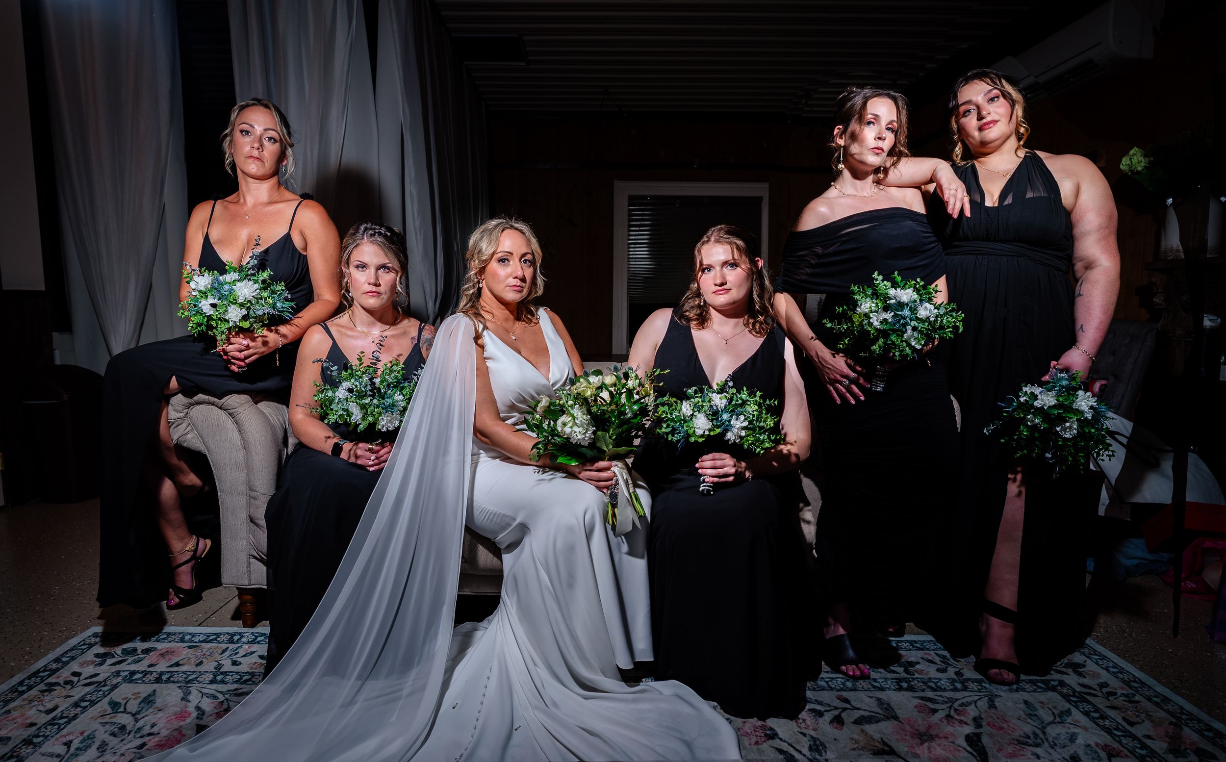 Bride in white gown with veil poses with five bridesmaids in black dresses holding green bouquets.