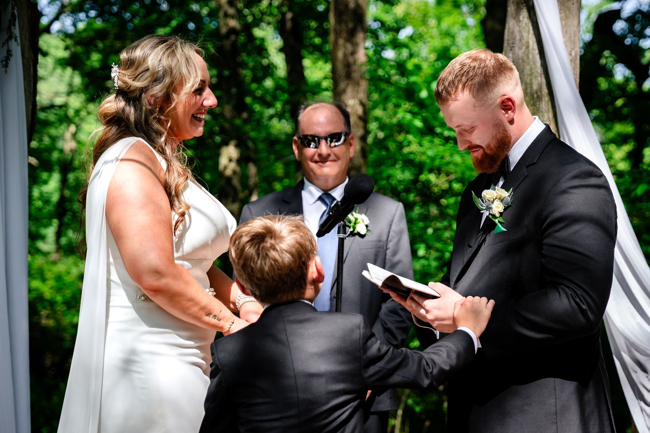 Bride and groom exchange vows outdoors with officiant and child present at an intimate garden wedding ceremony.