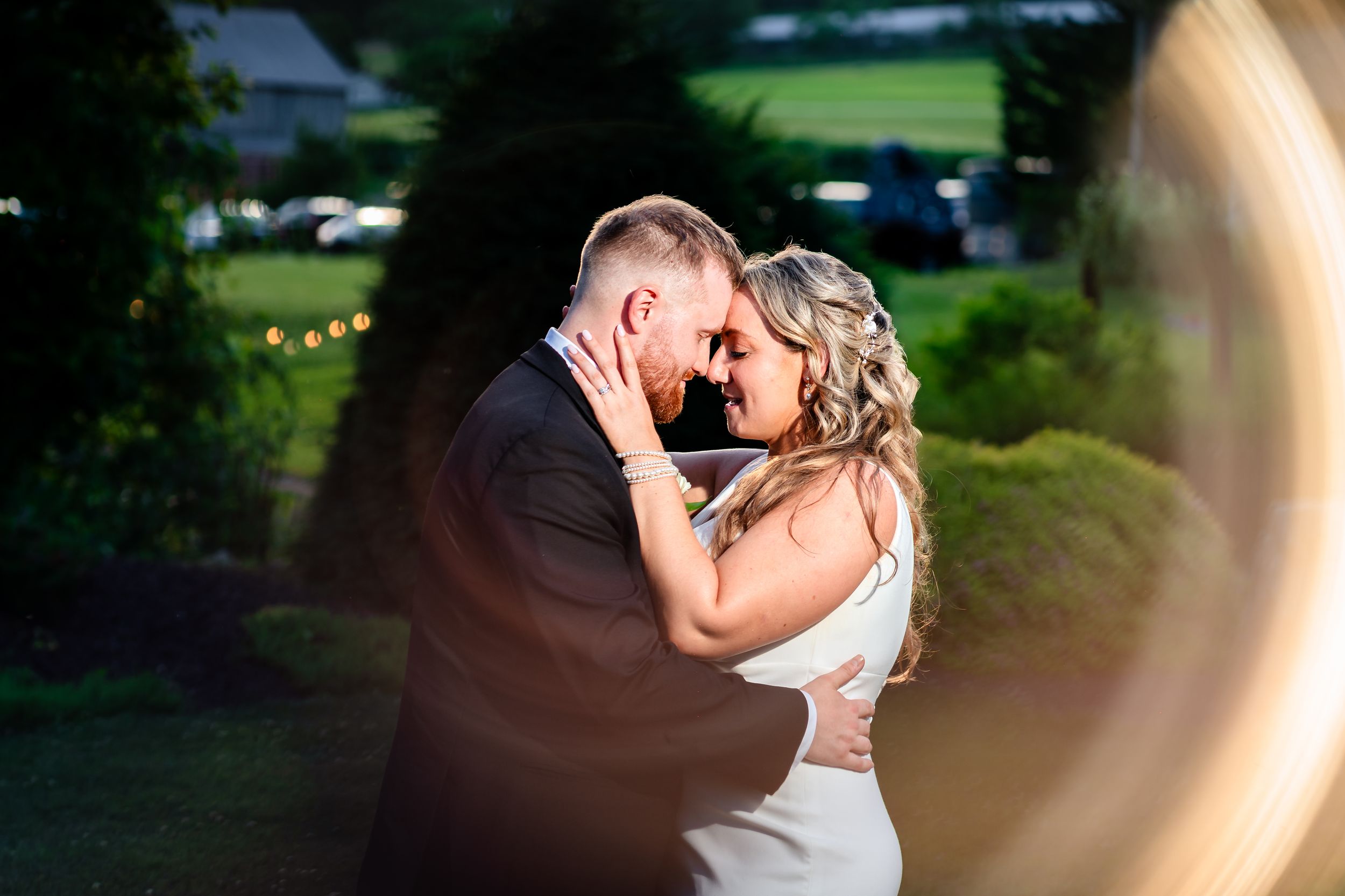 Newlyweds share romantic embrace at dusk surrounded by lush garden greenery.