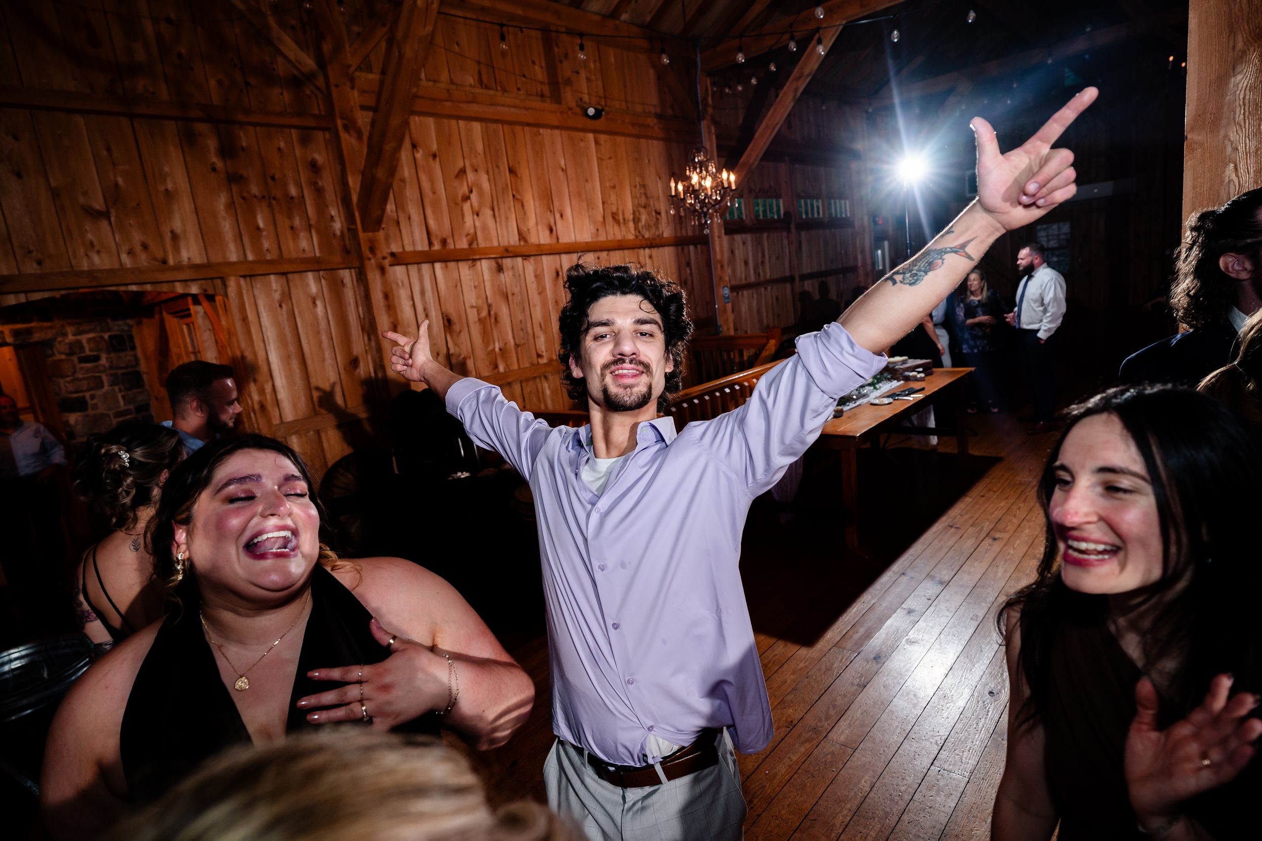 Guest celebrates on dance floor with arms raised in rustic barn wedding reception venue.
