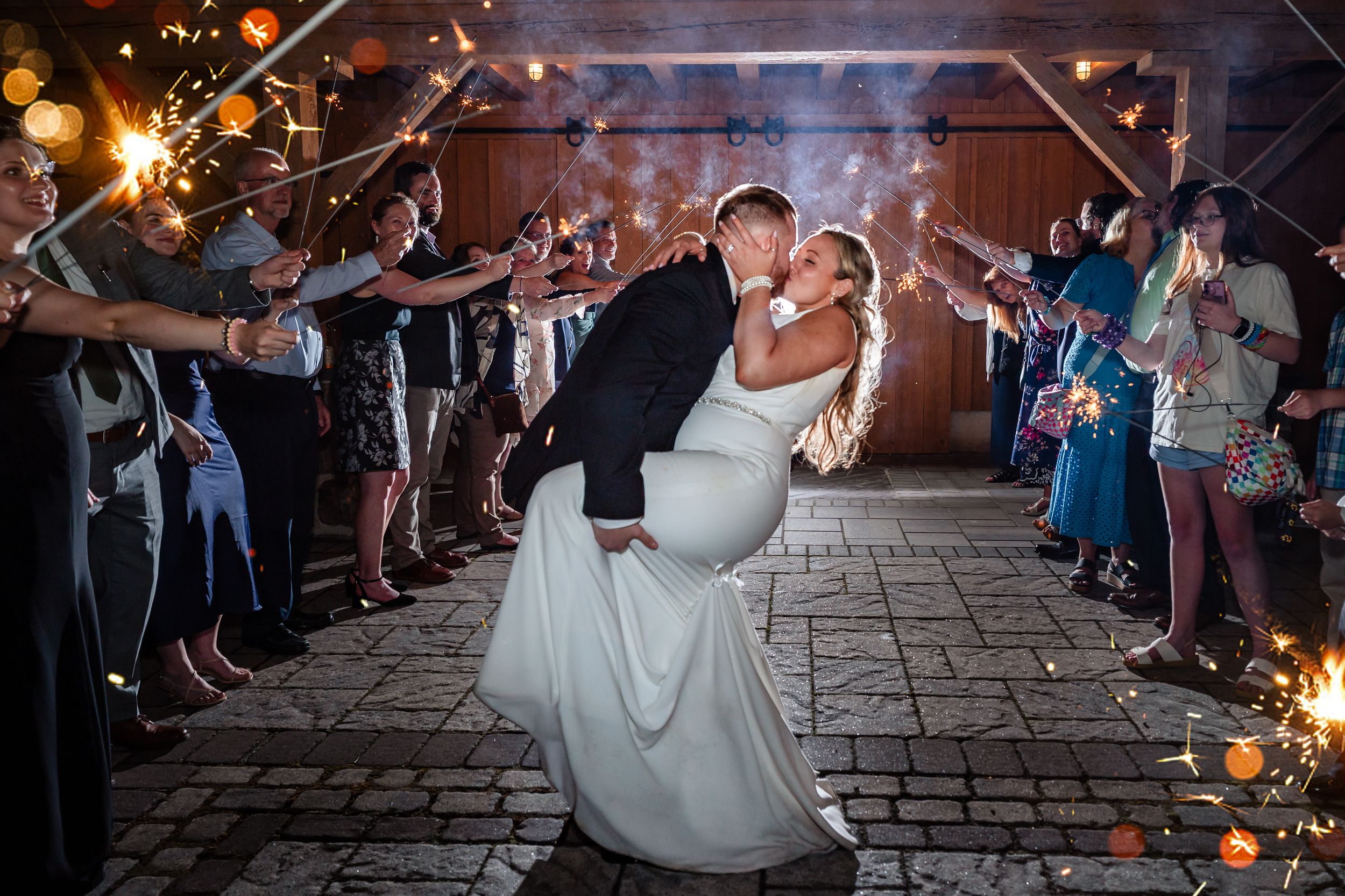 Groom dips bride for a kiss during sparkler exit at romantic rustic barn wedding celebration.