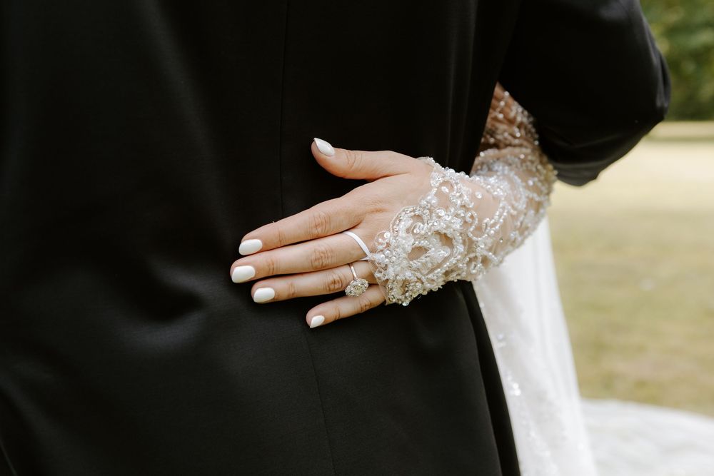 Bride's hand with white manicure and lace glove resting on groom's black suit jacket.