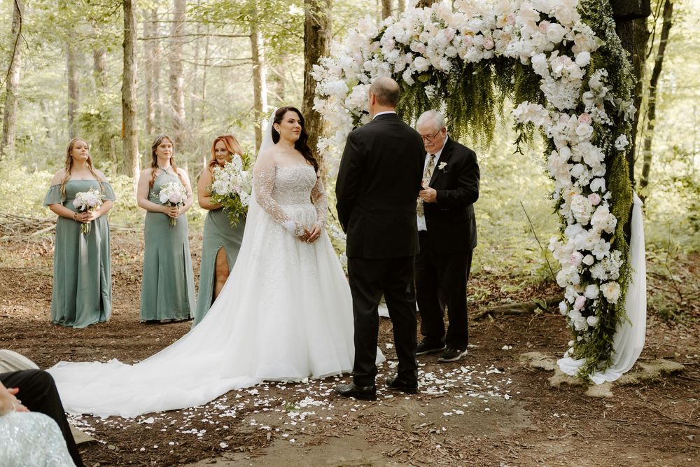 Bride and groom exchange vows at an outdoor forest wedding ceremony with floral arch.