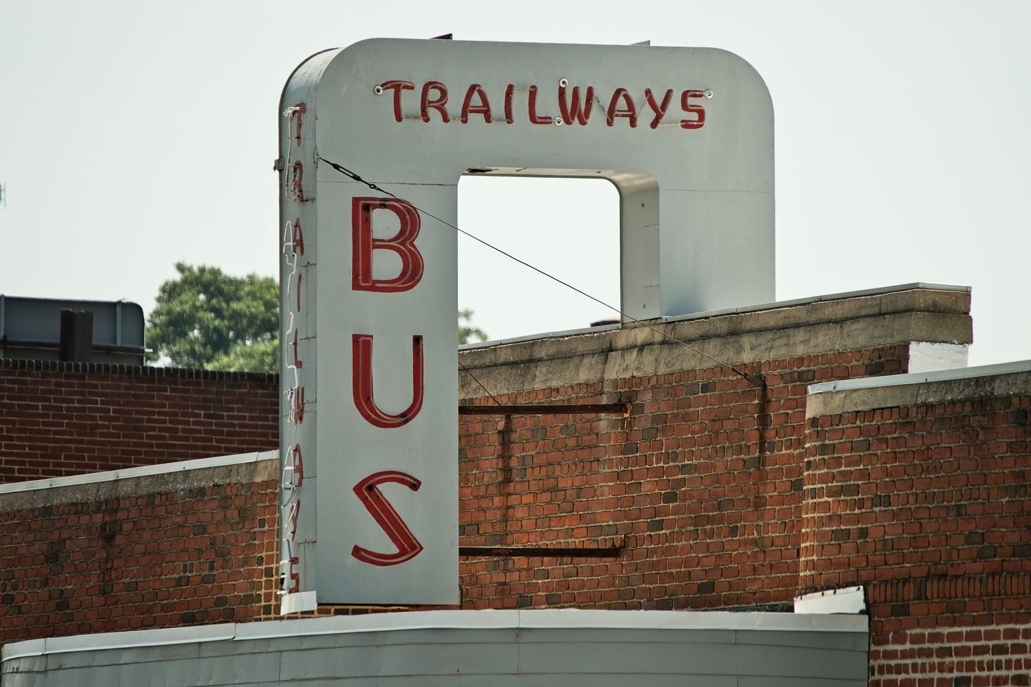 Vintage Trailways Bus station sign in red lettering mounted on a brick building exterior.