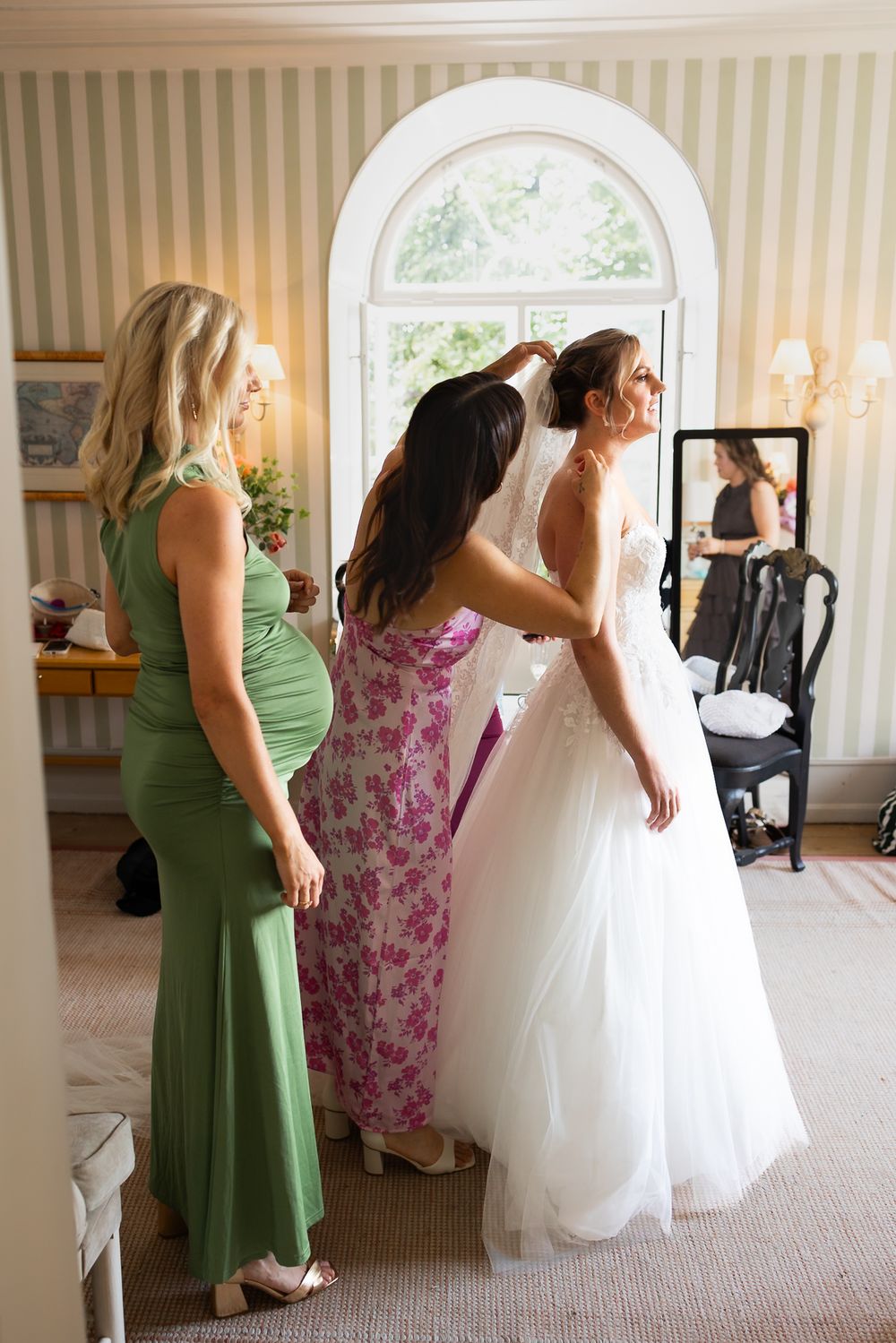Bride being helped into wedding dress by bridesmaids in elegant striped room before ceremony.