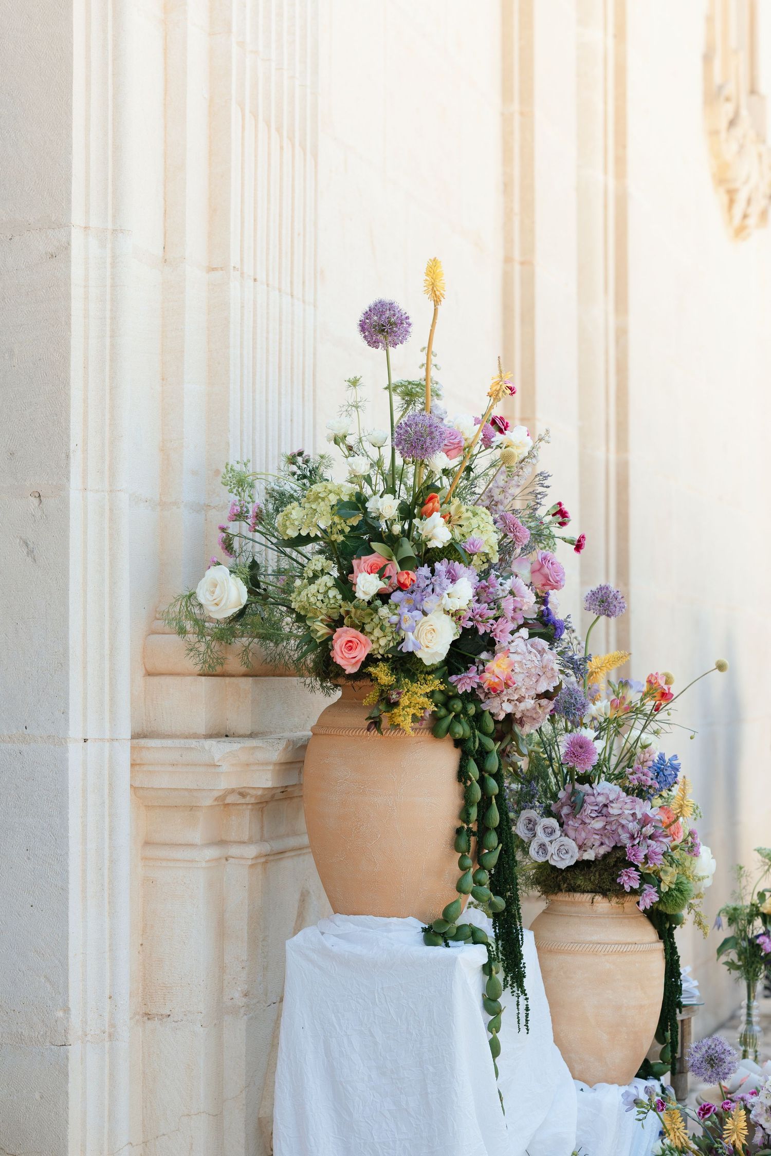 Two large terracotta urns filled with colorful wildflower arrangements against a stone column backdrop.